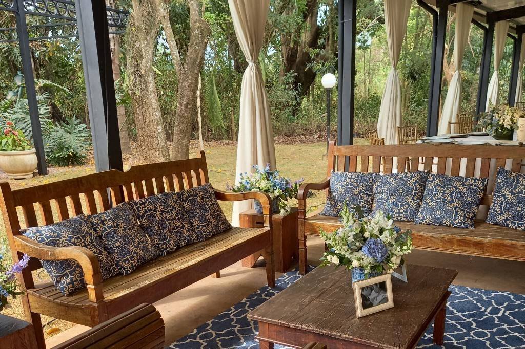 Lounge coberto com bancos de madeira e almofadas azuis, aberto para o jardim