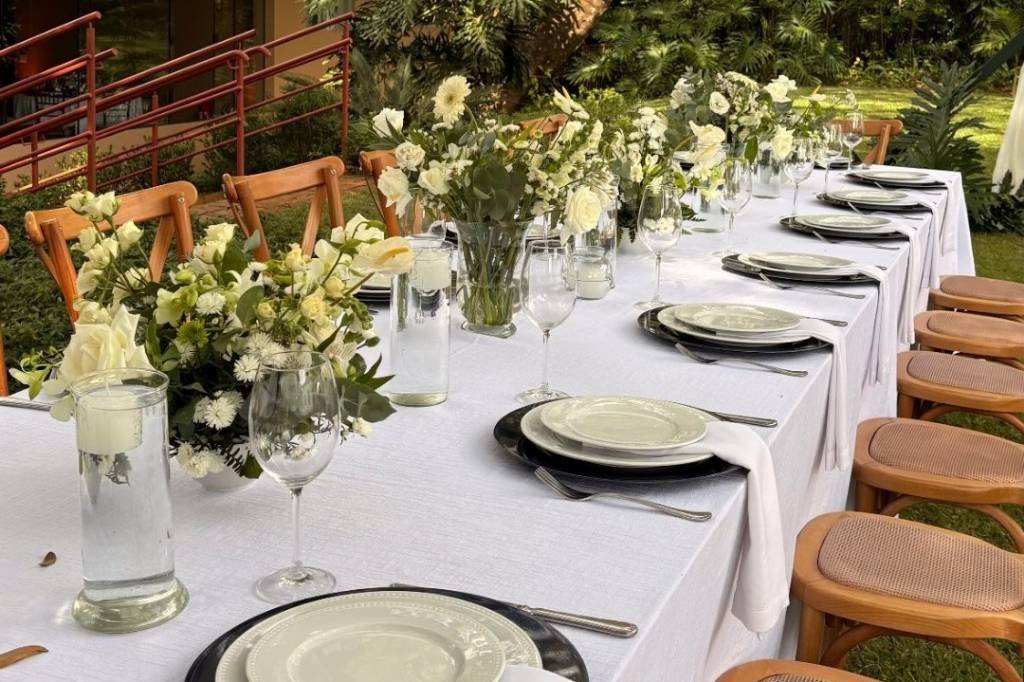 Mesa imperial posta no jardim, com arranjos brancos e cadeiras de palhinha