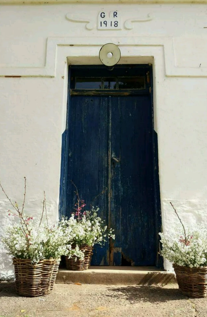 A porta principal azul, com a inscrição GR 1918 acima e cestos de flores brancas na soleira